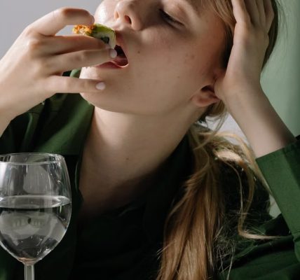 Portrait of a young woman savoring sushi with a wine glass in a relaxed, green-themed setting.