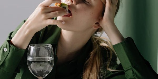 Portrait of a young woman savoring sushi with a wine glass in a relaxed, green-themed setting.